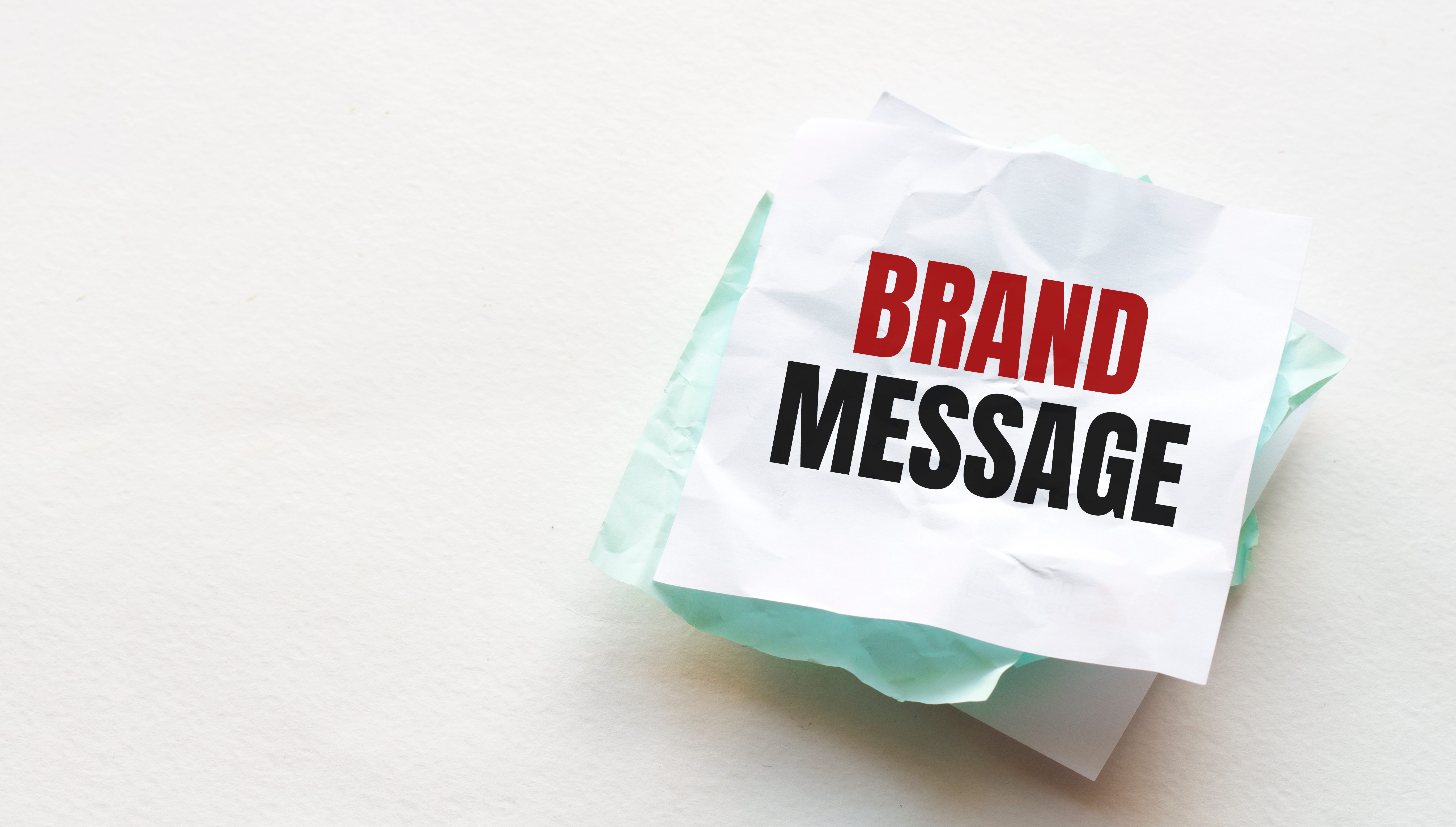 notebook and pen on a wood table, copy space for text, female hand writing BRAND MESSAGE on crumpled yellow paper, work place, brainstorming